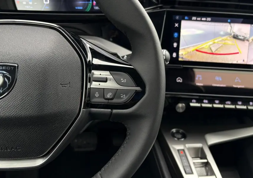 Vue rapprochée du volant noir de la Peugeot 308 SW Hybrid 2025 avec commandes intégrées et écran tactile affichant la caméra de recul.