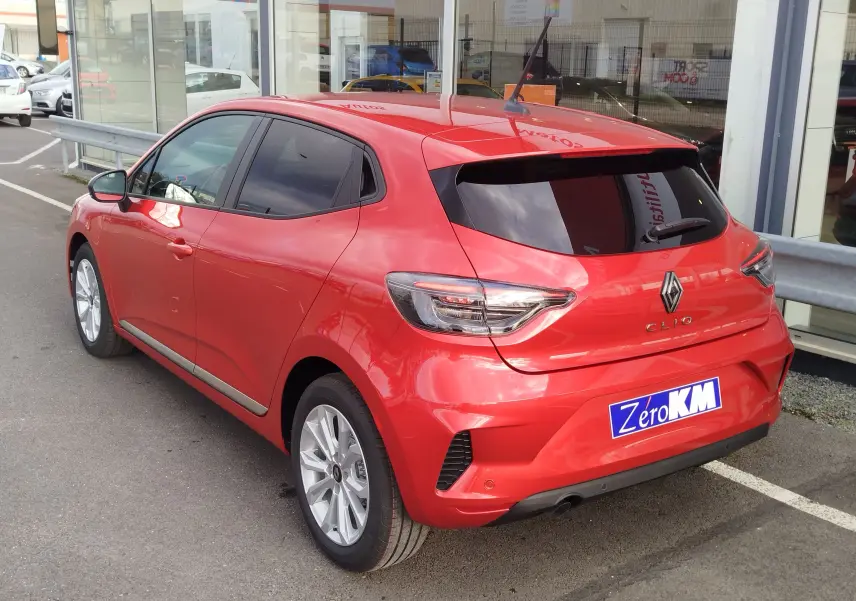 Vue 3/4 arrière droite d'une Renault Clio rouge flamme 2025 avec vitres teintées et jantes alliage argentées.