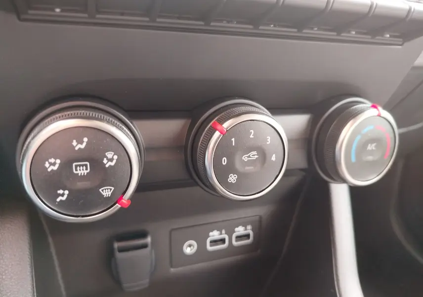 Gros plan sur les commandes de climatisation et ventilation de la Renault Clio rouge flamme, avec réglages précis et ports USB visibles.