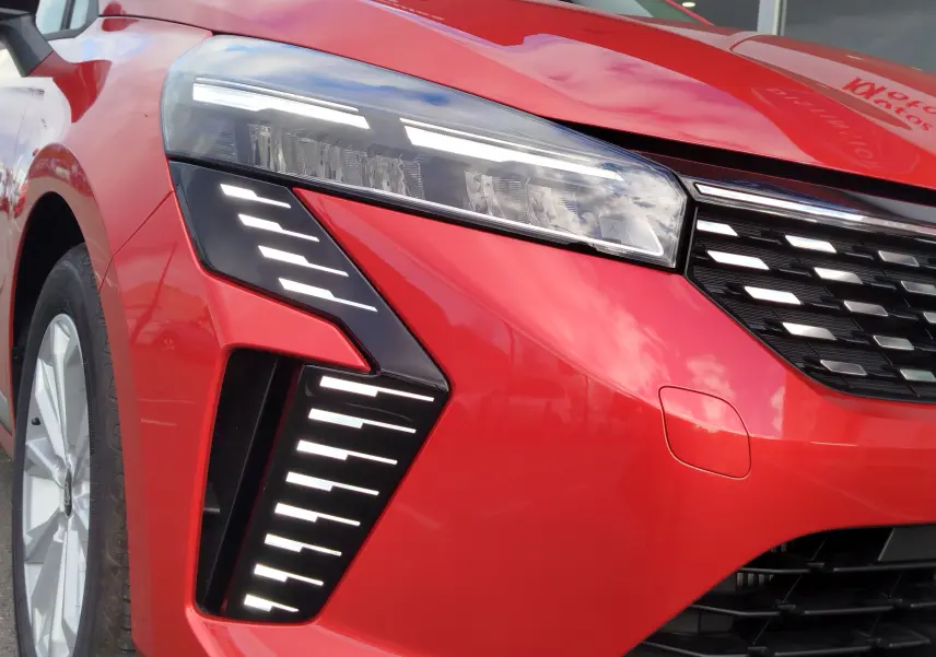 Gros plan sur l'avant gauche de la Renault Clio TCE 90CH X-TRONIC Evolution rouge flamme avec ses phares LED distinctifs.