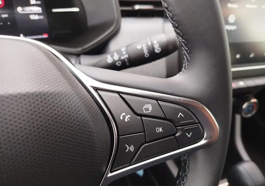 Gros plan sur les commandes au volant côté droit de la Renault Clio rouge flamme 2025, avec boutons multifonctions et finition cuir noire.