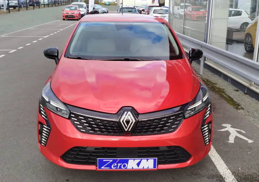 Vue frontale d'une Renault Clio rouge flamme 2025 avec calandre noire et feux LED verticaux allumés.