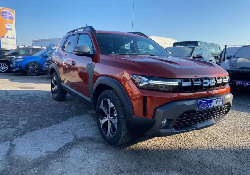 Dacia Duster brun terracotta en 3/4 avant droit, avec jantes alliage 18 pouces et barres de toit noires.