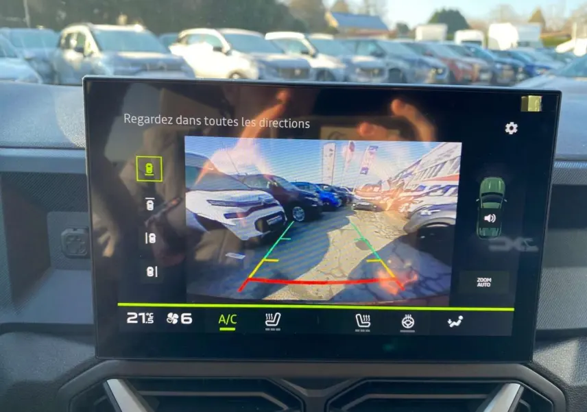 Écran de caméra de recul du Dacia Duster 2024 montrant un parking ensoleillé avec plusieurs véhicules visibles.