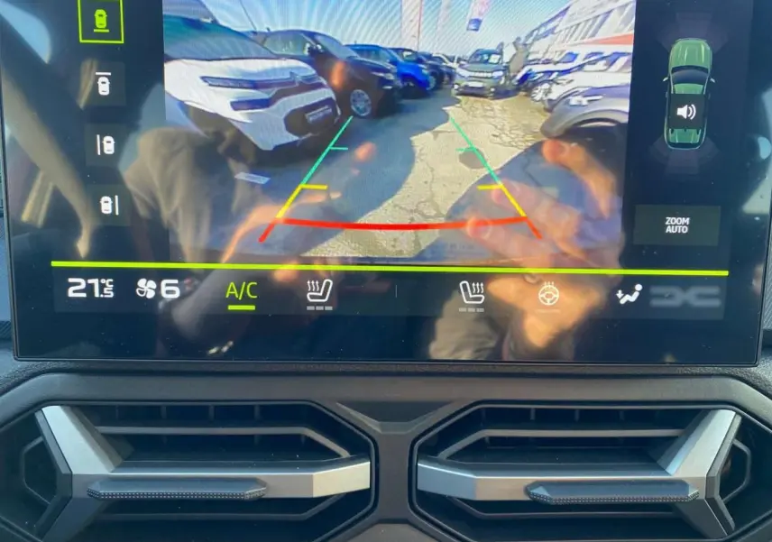 Vue écran caméra de recul du Dacia Duster 2024 brun terracotta montrant un parking avec plusieurs véhicules.