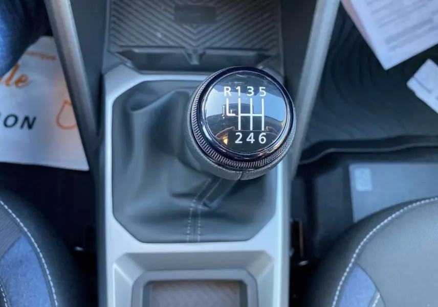 Le levier de vitesses manuel du Dacia Duster 2024 vu de dessus, entouré de sièges gris et bleu.