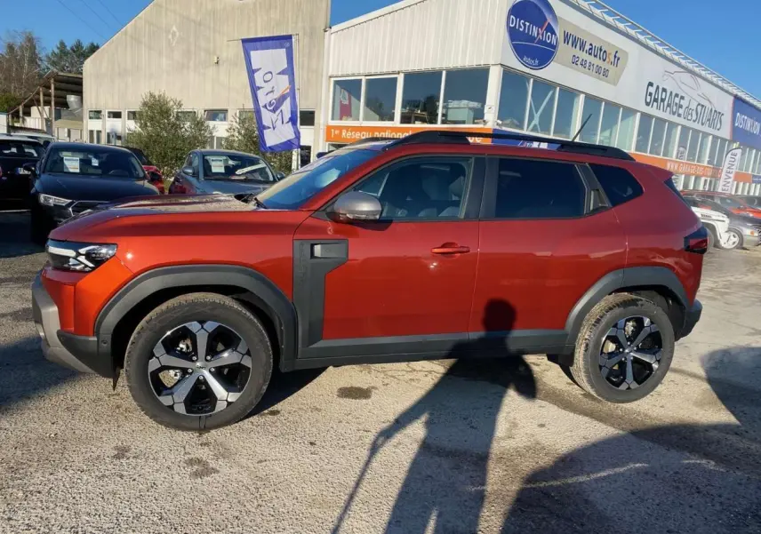 Profil côté gauche du Dacia Duster 2024 brun terracotta avec barres de toit noires et jantes alliage 18 pouces.