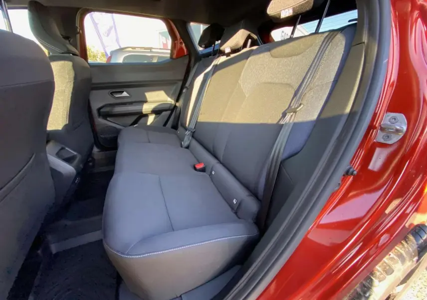 Vue côté droit des sièges arrière noirs du Dacia Duster 2024 brun terracotta avec porte ouverte au soleil.