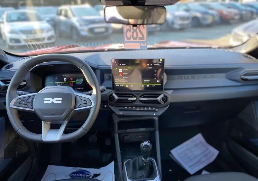 Vue intérieure avant du tableau de bord du Dacia Duster 2024 avec volant multifonction et écran tactile central.