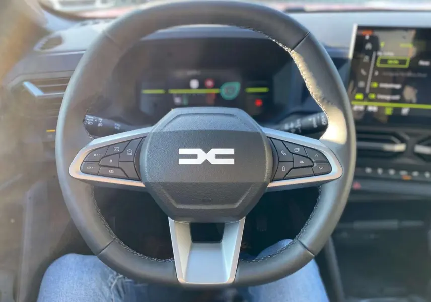Volant multifonction du Dacia Duster 2024 vu de face, avec tableau de bord digital et écran central en arrière-plan.
