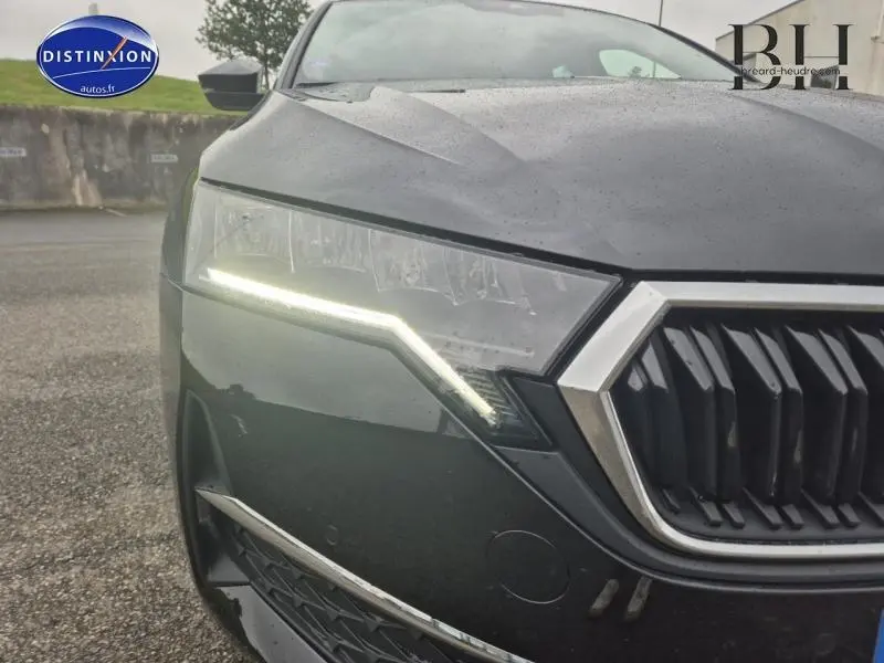 Gros plan sur le phare avant gauche allumé et la calandre chromée d'une Skoda Octavia Combi noire nacrée 2024