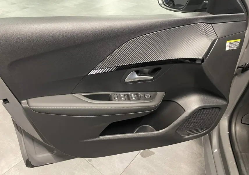Vue intérieure côté gauche de la porte avant gris sélénium de la Peugeot 208 avec insert carbone et commandes de vitres.