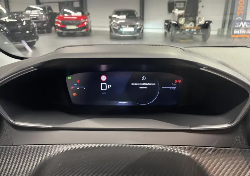 Vue rapprochée du combiné numérique Peugeot 208 hybride 2025 avec affichage digital et décor carbone autour.