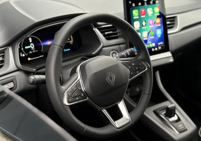 Vue rapprochée du volant noir et du tableau de bord numérique du Renault Captur 2025 avec écran tactile central allumé.