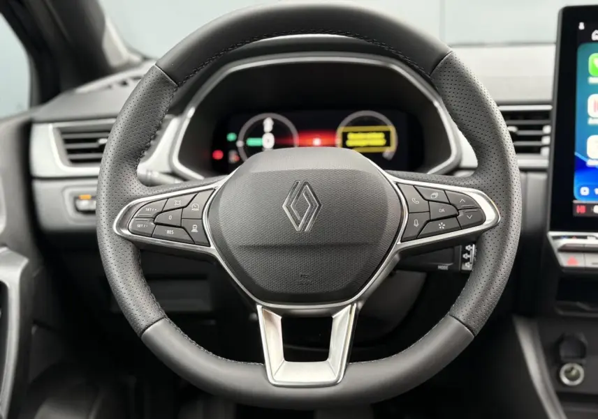 Vue rapprochée du volant noir perforé avec commandes intégrées du Renault Captur 2025, tableau de bord numérique en arrière-plan.