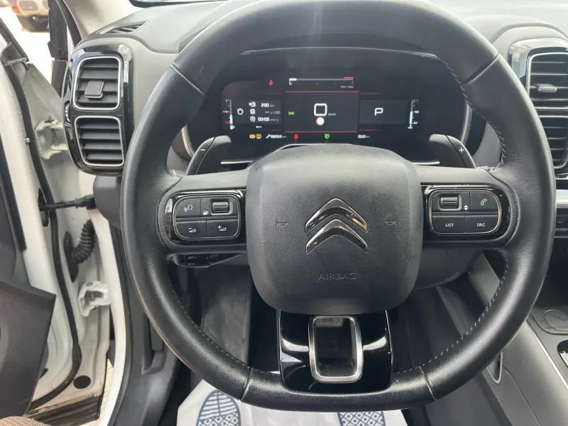 Volant cuir noir avec commandes multifonctions dans un Citroën C5 Aircross blanc, vue centrée sur le poste de conduite.