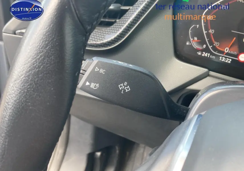 Gros plan sur la commande de clignotants à gauche du volant d'une BMW Série 1 gris foncé, tableau de bord visible.