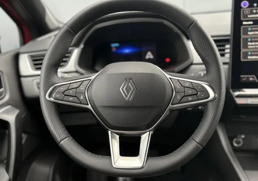 Vue rapprochée du volant en cuir noir perforé du Renault Captur 2025 avec commandes intégrées et tableau de bord numérique flou.