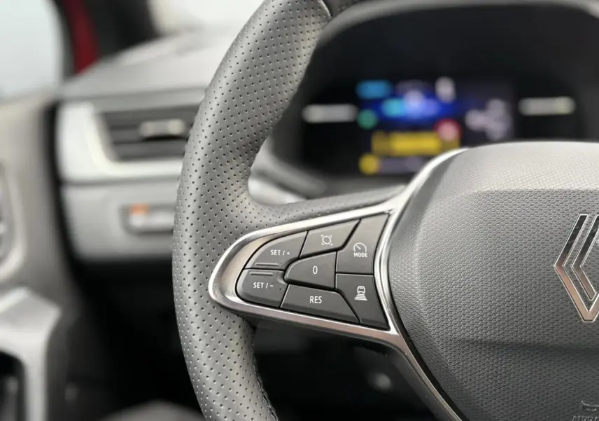 Gros plan sur le volant perforé gris du Renault Captur 2025 avec commandes intégrées et tableau de bord numérique flou.