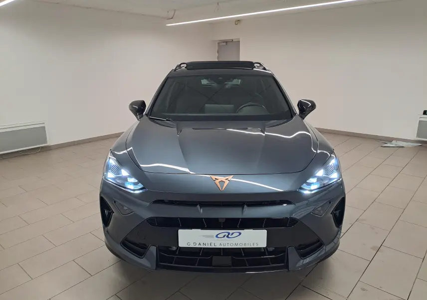 Vue frontale d'une CUPRA Formentor gris magnétique avec phares allumés et logo cuivré sur le capot.