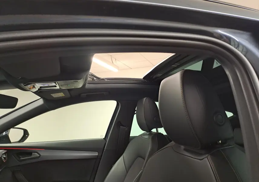 Vue intérieure côté conducteur du CUPRA Formentor gris magnétique, mettant en valeur le toit ouvrant panoramique et les sièges en cuir noirs.
