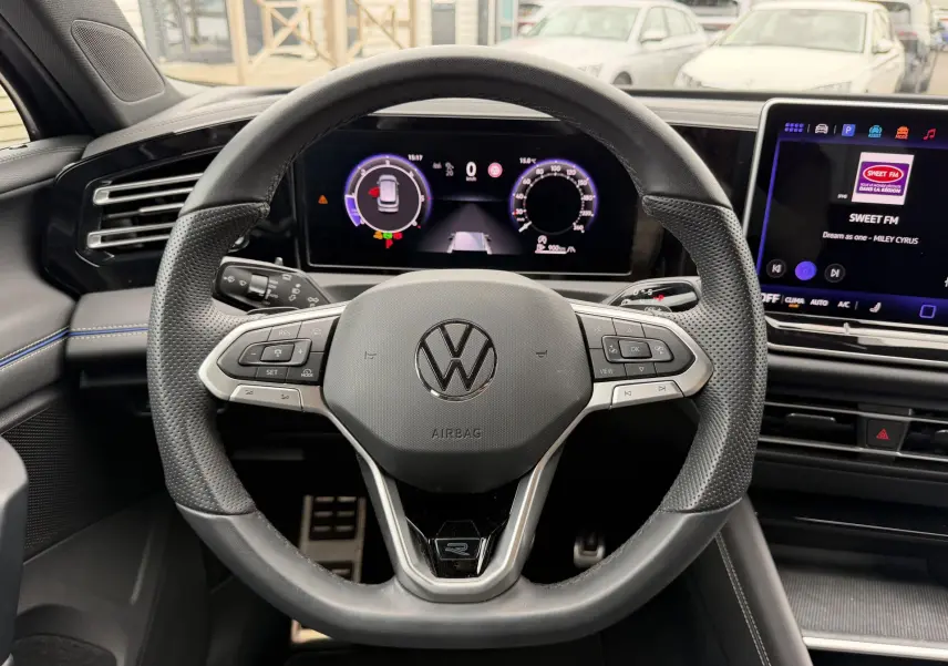 Vue intérieure centrée sur le volant cuir noir du Volkswagen Tiguan 2025 avec tableau de bord numérique et écran tactile.