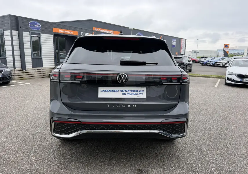 Vue arrière d'un Volkswagen Tiguan gris métallisé avec feux arrière LED et logo VW centré sur un parking extérieur.