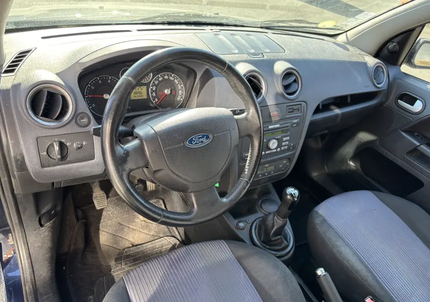 Vue intérieure côté conducteur de la Ford Fusion 2009 bleu, montrant le volant, tableau de bord et levier de vitesses manuel.