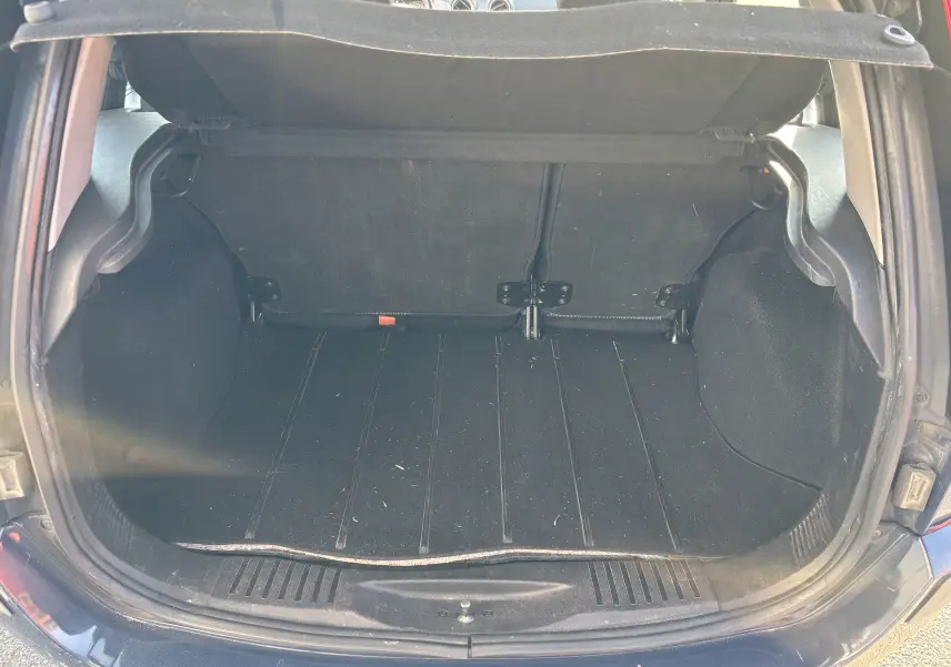 Coffre ouvert vu de l'arrière d'une Ford Fusion bleu 2009, montrant l'espace de chargement vide et la moquette noire.