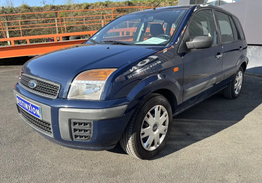 Ford Fusion bleu vue 3/4 avant droit, compacte cinq portes avec pare-chocs noir et jantes acier.