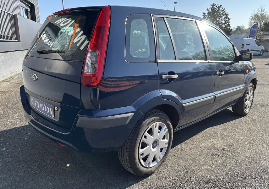 Ford Fusion bleu vue 3/4 arrière droit, compacte 5 portes avec feux arrière verticaux et jantes argentées.