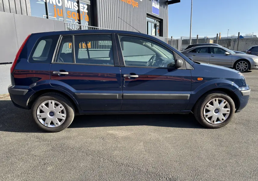 Ford Fusion bleu vue de profil côté gauche, compacte 5 portes avec jantes acier et enjoliveurs d'origine.
