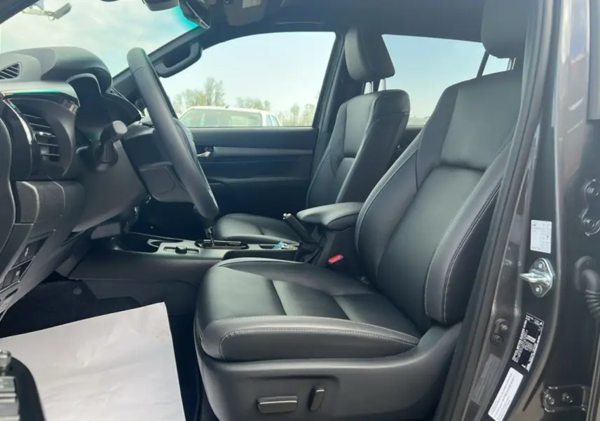 Intérieur du Toyota Hilux 2025 gris atlas, vue côté conducteur ouverte, sièges avant en cuir noir avec coutures blanches.