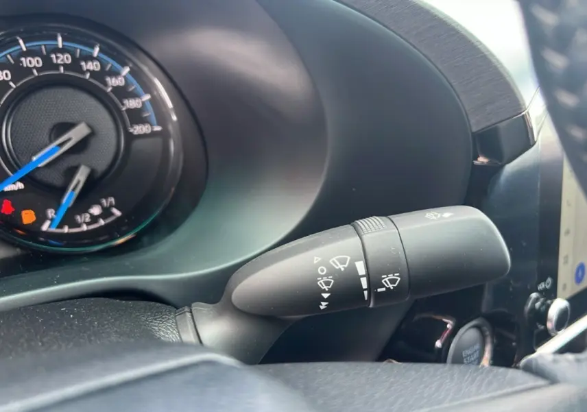 Gros plan sur la commande d'essuie-glace du Toyota Hilux 2025 gris atlas, avec tableau de bord et bouton démarrage visibles.