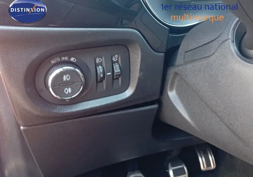 Gros plan sur les commandes d'éclairage et les pédales côté conducteur de l'Opel Corsa rouge métal 2023.