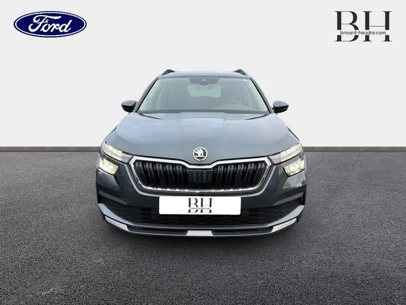Vue frontale d'un Skoda Kamiq 1.0 TSI Business gris Météore avec calandre chromée et phares LED allumés.