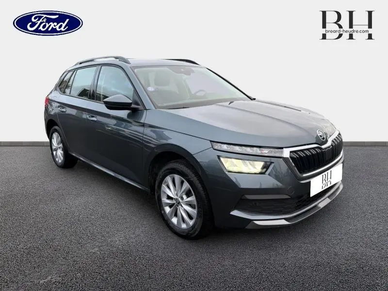 Vue 3/4 avant droit d'un SKODA KAMIQ gris météore avec calandre chromée et phares LED allumés.