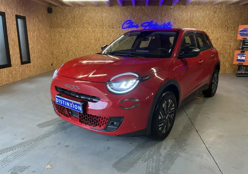 Vue 3/4 avant d'une FIAT 600 rouge 2024 avec phares allumés, calandre noire et jantes stylisées en intérieur bois.