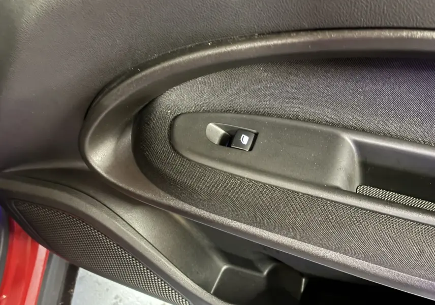 Gros plan sur la commande de lève-vitre noir intégrée à la porte côté gauche d’une FIAT 600 rouge 2024.