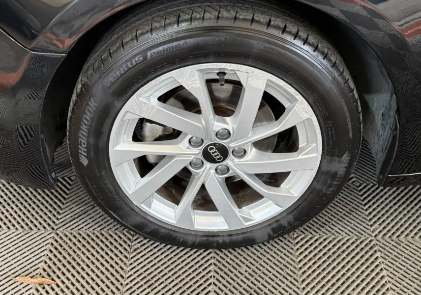 Gros plan sur la roue avant droite d’une Audi A1 noire, avec jante argentée et logo Audi au centre.