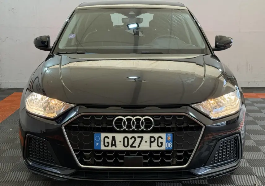 Vue frontale d'une Audi A1 noire 2021 avec calandre hexagonale et phares allumés dans un garage.