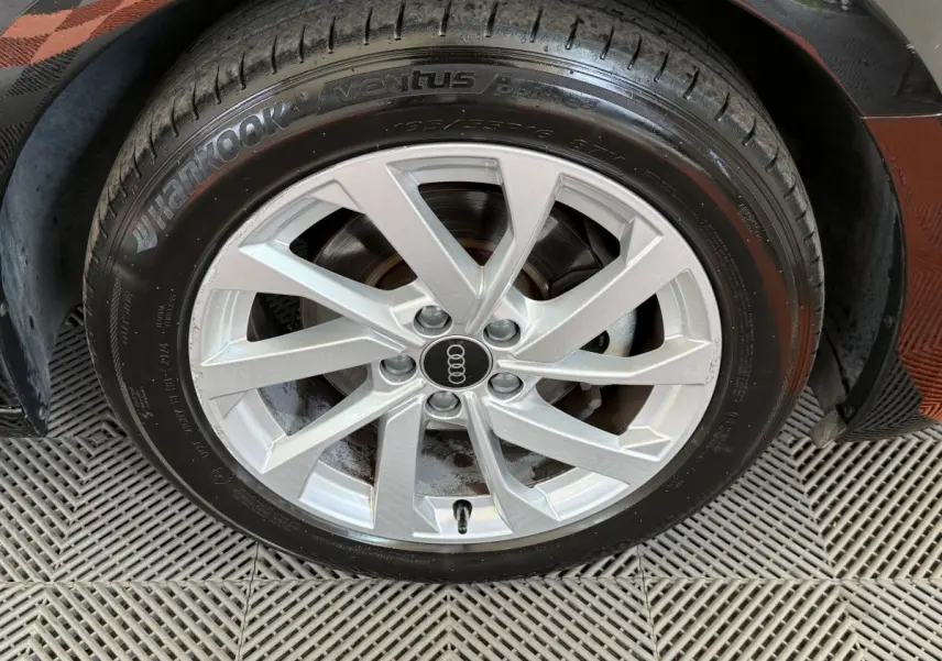 Gros plan sur la jante argentée avec logo Audi d'une Audi A1 noire, vue côté roue avant droite.