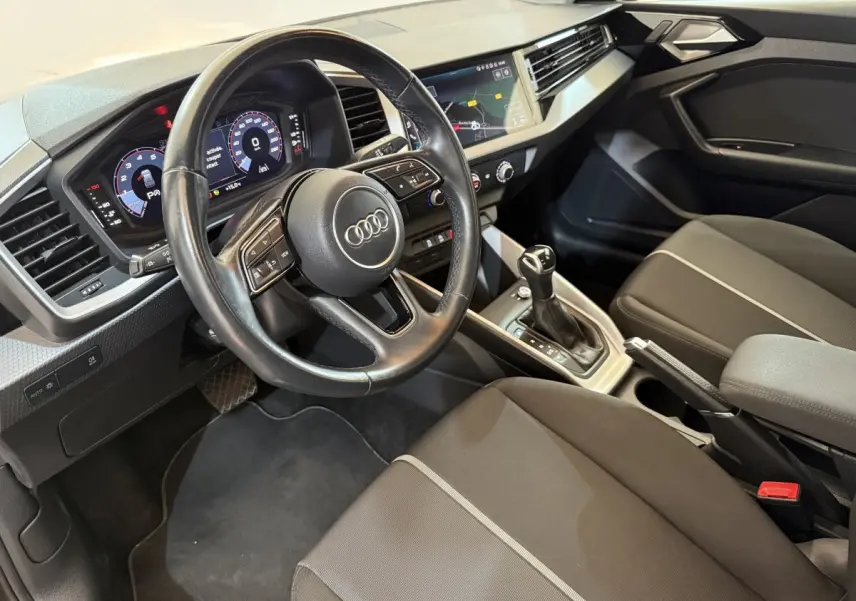 Vue intérieure côté conducteur de l'Audi A1 2021 noir, volant cuir multifonctions et tableau de bord digital.