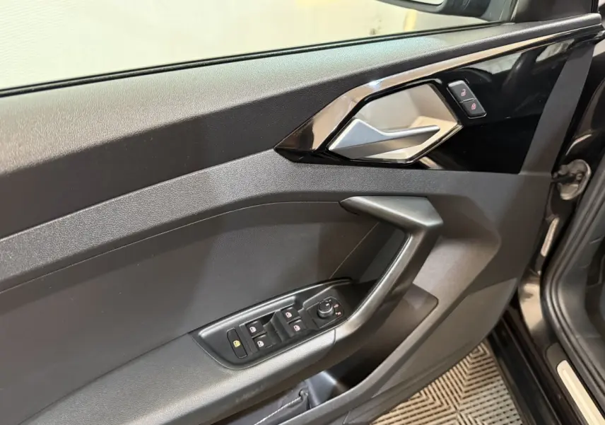 Intérieur côté conducteur de l'Audi A1 noir, montrant la porte avec commandes des vitres et poignée argentée.