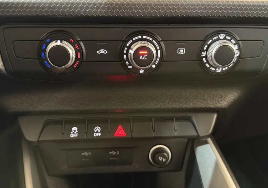 Vue rapprochée du tableau de bord de l’Audi A1 2021 noir, montrant les commandes de climatisation et boutons de sécurité.