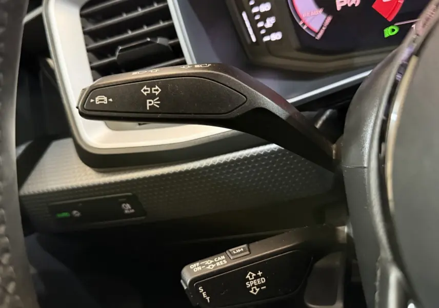 Gros plan sur les commandes au volant de l’Audi A1 noire, avec levier de clignotants et régulateur de vitesse visibles.