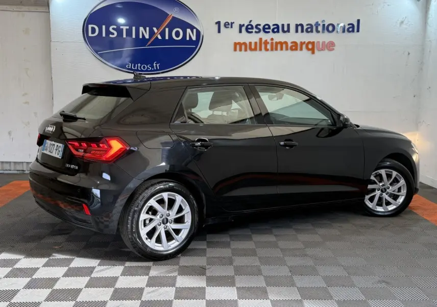 Audi A1 noire vue de profil côté droit, avec jantes argentées et feux arrière allumés en intérieur showroom.