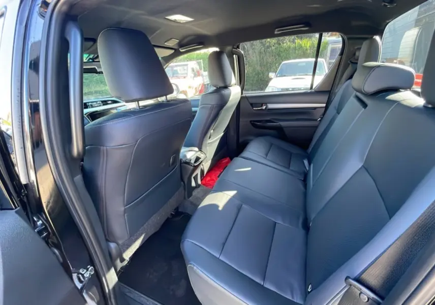 Vue intérieure arrière côté gauche du Toyota Hilux 4x4 2025 Noir Attitude avec sièges en cuir noir et espace spacieux.