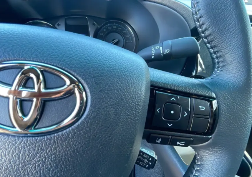 Gros plan sur le volant en cuir noir du Toyota Hilux 2025 avec commandes intégrées et logo chromé visible.