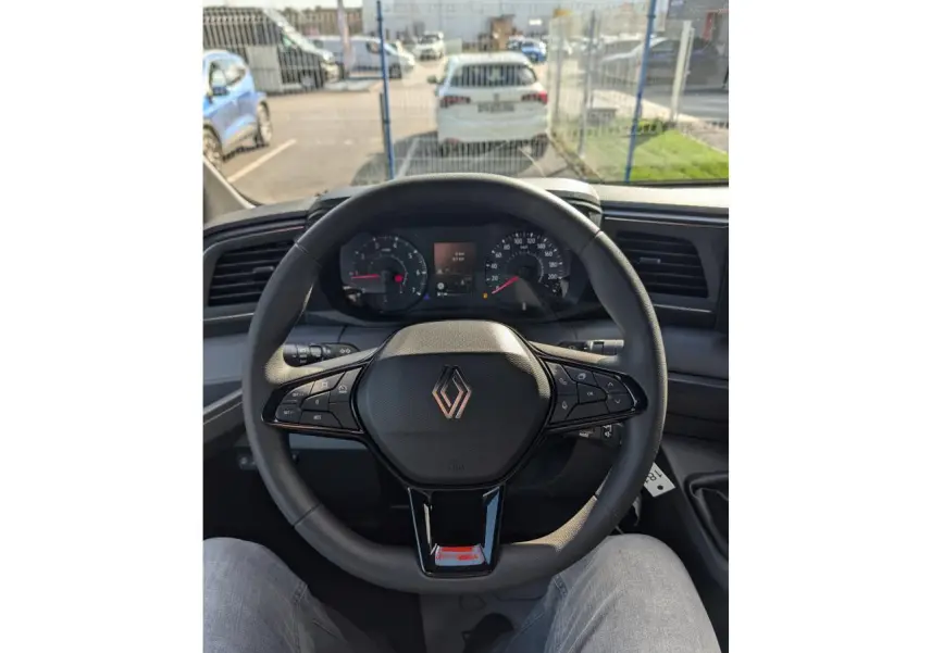Volant noir avec logo Renault au centre, tableau de bord digital et compteur analogique, vue depuis le siège conducteur du Renault Master 2025.